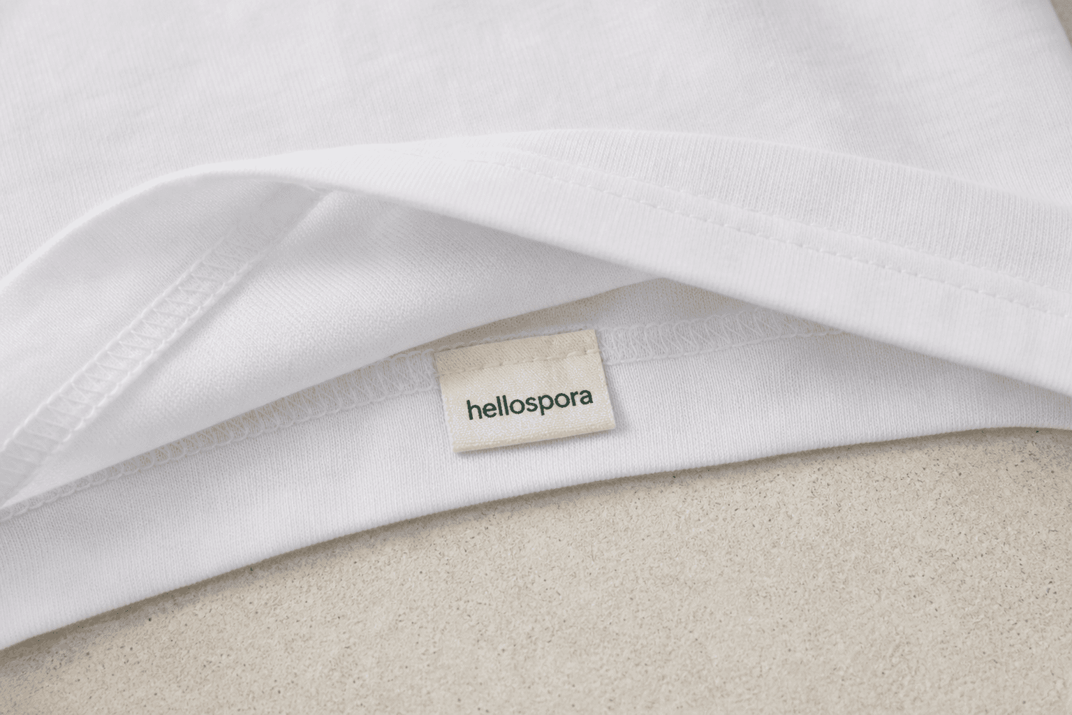 Back bottom hem of The First Tee flipped up to show the lowercase hellospora tag